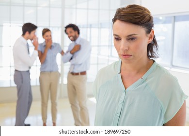 Colleauges gossiping with sad young businesswoman in foreground at a bright office - Powered by Shutterstock