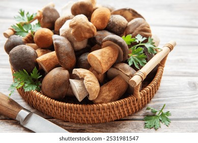 A collection of assorted fresh mushrooms is beautifully arranged in a woven basket, accompanied by a knife and vibrant herbs on a wooden table, showcasing nature's bounty. - Powered by Shutterstock