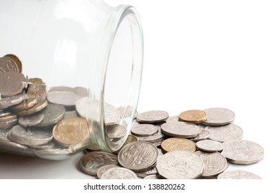 Collection of Australian coins spilling out of a glass jar tipped on its side