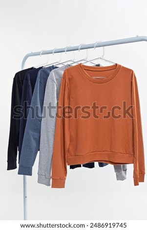 collection of basic premium cotton t-shirts hanging on clear hangers. Ideal for mockup design, minimalist details and realistic colors. Male and female models, without print or brand. Clean design.