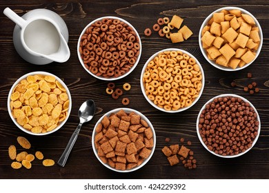 Collection of breakfast cereal on a wooden background. Cornflakes, corn pads, rings and balls. 