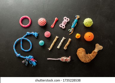 Collection Of Colorful Shabby Dog’s Toys On Black Chalkboard Background. Balls, Dogchews, Sticks And Rope Captured From Above (top View, Flat Lay).