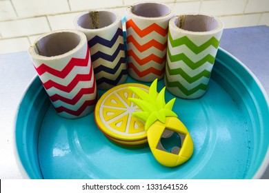 Collection of colourful chevron-striped fabric beer stubby holders on a blue metal tray with yellow lemon coasters and a pineapple shaped beer bottle opener.