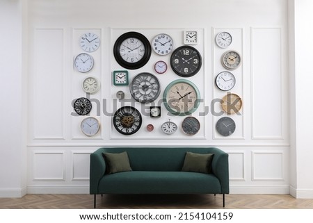 Collection of different clocks and comfortable sofa in stylish room. Interior design