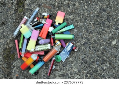 A collection of discarded electronic cigarette vapes have been collected and placed together over a worn concrete floor