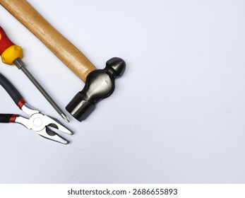A collection of essential hand tools, including a screwdriver, a ball-peen hammer, and pliers, is diagonally arranged on a clean white background with large copy space.