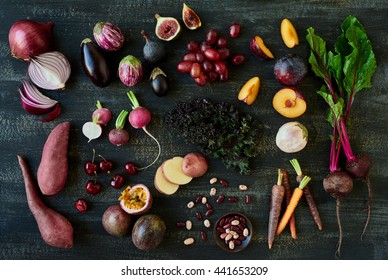 Collection Of Fresh Purple Toned Vegetables And Fruits On Dark Rustic Distressed Background, Heirloom Carrots, Beetroot, Fig, Aubergine, Grapes, Radishes, Loose Leaf Lettuce, Kale, Beans 