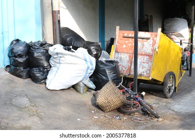 A Collection Of Garbage In Plastic Bags Piled In The Corner Of The Yard Next To A Yellow Garbage Cart