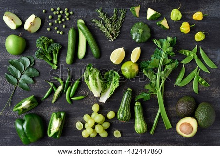 Collection of green vegetables produce on dark background, broccolini, avocado, squash, chilli, grapes part of flat lay overhead set