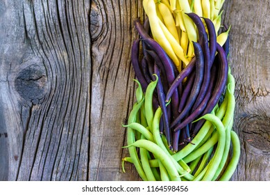Collection of green, yellow and purple bush beans, opened green peas on wooden rustic background.