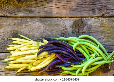 Collection of green, yellow and purple bush beans, opened green peas on wooden rustic background.