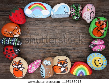 A collection of happy, colorful hand painted cartoon animal rocks are framing a wood plank background.