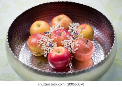 Collection of healthy organic fresh red apples decorated with dainty white elder flowers in a bowl to be eaten as a delicious summer snack or used as cooking ingredients