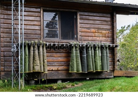 Collection of hip waders hanging up drying outside on a rustic wood cabin
