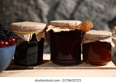 Collection Of Homemade Berry Jam From Red Currant, Cherries And Blackcurrant On A Wooden Surface, With A Blurred Blue Bowl With Fresh Ripe Berries In The Foreground. Canned Food, Canning For Winter