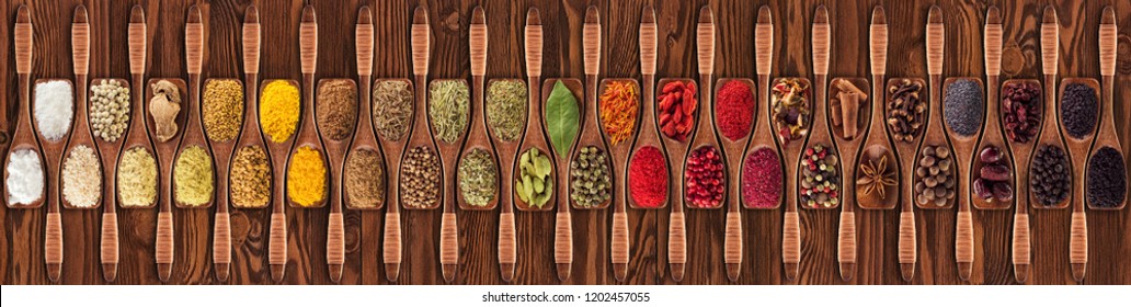Collection of Indian condiments and herbs in wooden spoons, top view. Spices for eating on kitchen table as food packaging background.