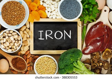 Collection iron rich foods as liver, buckwheat, eggs, parsley leaves, dried apricots, cocoa, lentil, bean, blue poppy seed, broccoli, dried mushrooms, peanuts and pistachios on wooden table.