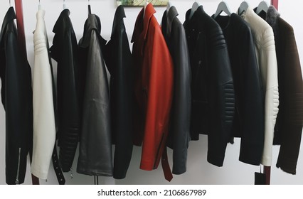 Collection of many new women's leather spring jackets on hangers in the shop. Background and closeup texture of elegant brown, white, black and red leather jackets.