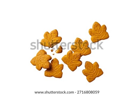 A collection of maple leaf shaped ginger cookies are scattered across a clean white background. One cookie is broken, revealing its crumbly interior. The...