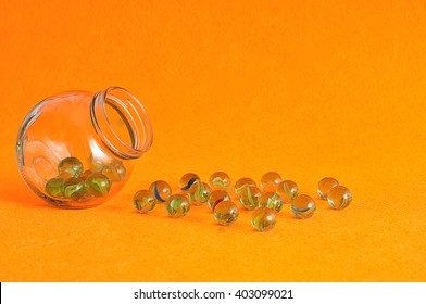 A Collection Of Marbles In A Glass Jar Displayed On An Orange Background