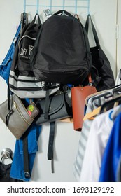 Collection Of Multiple Backpacks, Handbags And A Pair Of Jeans Stacked And Hanging On A Rack Behind The Door At Home.