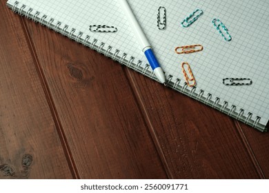 A collection of notebooks and colorful paperclips arranged on a wooden desk. - Powered by Shutterstock