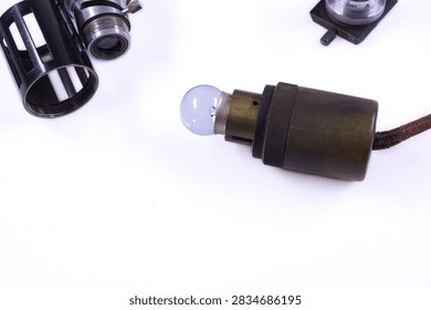 Collection of old microscope components with optical tubes, eyepieces, lenses and metal adjustment parts arranged on a white surface.