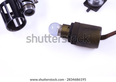 Collection of old microscope components with optical tubes, eyepieces, lenses and metal adjustment parts arranged on a white surface.