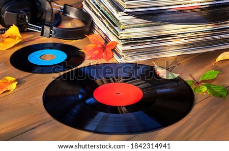 Collection of old vinyl records in a stack with headphones and autumn leaves.
