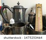 A collection of pewter jugs and tableware with a thermometer.