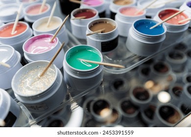 A collection of plastic jars filled with liquid nail polish, each one topped with a metal stick. They come in various colors and patterns, perfect for creating nail art in the city - Powered by Shutterstock