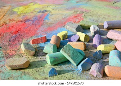 a collection of rainbow colored sidewalk chalk is scattered on the pavement outside, on top of a bright, colorful drawing