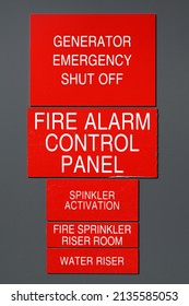 Collection of red and white fire emergency signs on gray wall featuring generator emergency shut off, fire alarm control, riser room