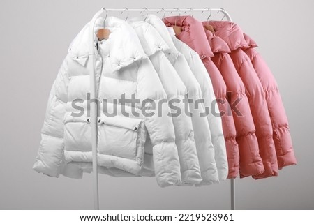 collection of stylish white and soft pink colours warm jackets hanging on wooden clothes hanger on metal clothing rack on white background. New autumn-winter fashion collection in store. copy space