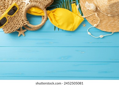 A collection of summer beach essentials including sunglasses, straw hat, and a yellow swimsuit arranged on a bright blue wooden surface, embodying the spirit of summer vacations and beach getaways - Powered by Shutterstock