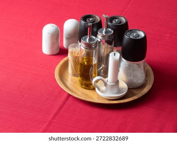 A collection of table condiments and a candle setting on a wooden tray, all resting on a red textured tablecloth.
