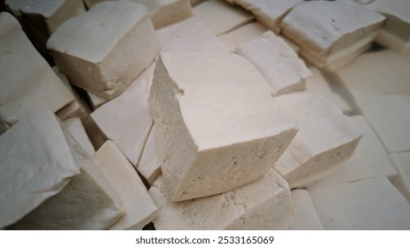 A collection of tofu blocks. They are white, smooth, and have a soft texture. The tofu is cut into uniform cubes and is commonly used as a versatile ingredient in various dishes.