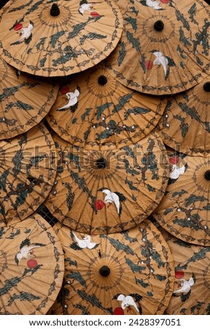 A collection of traditional Asian umbrellas featuring intricate design with painted white birds and green plants on a textured background vertical pattern