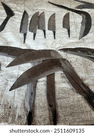 A collection of various metal blades
arranged on a white cloth surface. The
blades have different shapes and sizes,
with some featuring curved handles