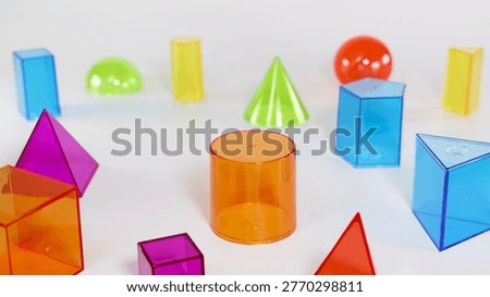 A collection of vibrant, translucent plastic 3D shapes including cylinders, pyramids, and spheres.
