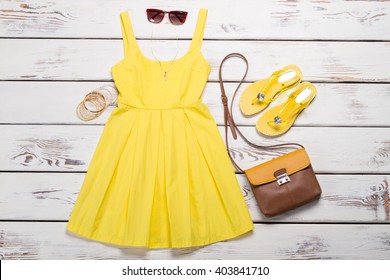 Collection of women's summer clothes. Yellow bright dress with accessories on wooden background.