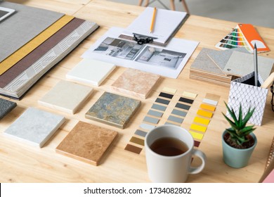 Collections of marble tiles, wallpapers, color swatches, photos of home interior, cup of tea, set of notepapers and domestic plant on desk
