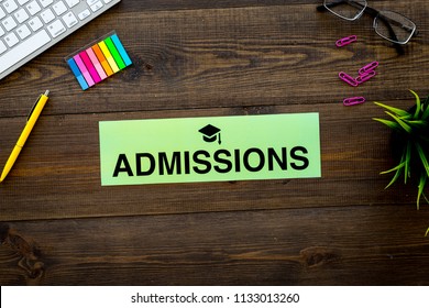 College Admission Concept. Word Admissions With Graduation Cap Sign On Dark Wooden Student Desk With Computer Top View Copy Space