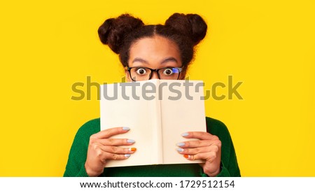 College Exams. Shocked black girl covering face with book, hiding behind it with eyes wide open. Panorama, copyspace