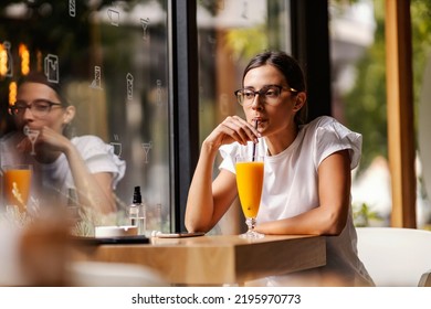 A College Girl Is Sitting In A Bar, Sipping Fresh Orange Juice On A Break Between Lectures. A Healthy Way To Kill Time. A Girl In A Bar Drinking Juice