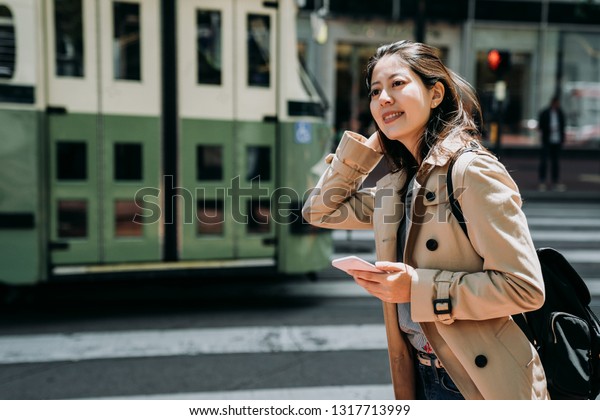 college girl study abroad sightseeing on weekend\
holidays. female teenager  holding cellphone searching plan route\
online map standing on road zebra crossing. green bus light train\
drive through.