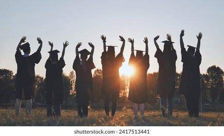 College graduates in robes waving at sunset. - Powered by Shutterstock