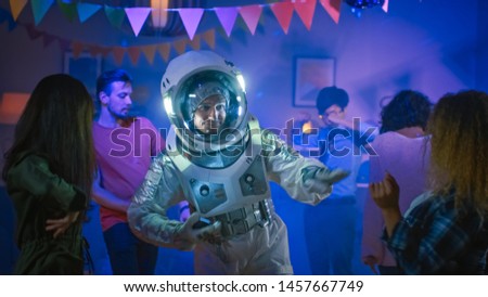 At the College House Costume Party: Fun Guy Wearing Space Suit Dances Off, Doing Robot Dance Modern Moves. With Him Beautiful Girls and Boys Dancing in Neon Lights.