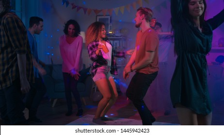 At The College House Party: Diverse Group Of Friends Have Fun, Dancing And Socializing. Boys And Girls Dance In The Living Room. Disco Neon Strobe Lights Illuminating Room.