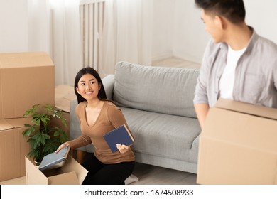 College Materials. Charming Asian Girl Giving Book To Her Friend While Packing For Moving In Or Out Of The Dorm